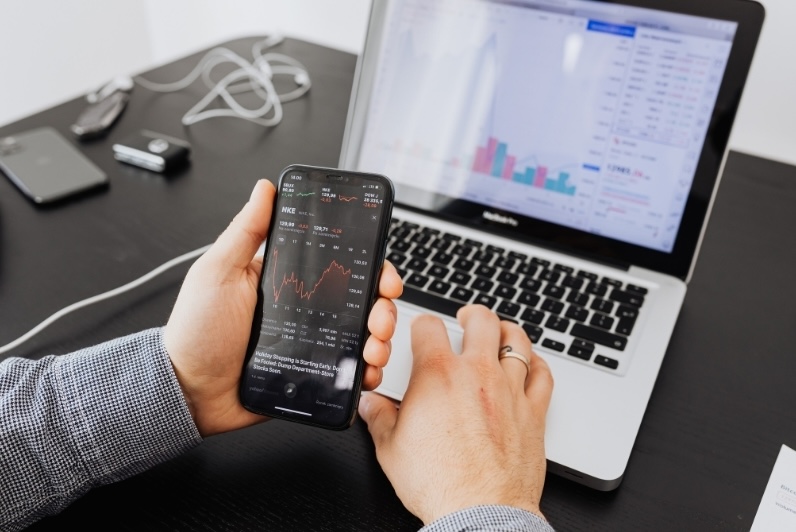 Person analyzing stock market data on a phone and laptop, illustrating the importance of tracking RSUs (Restricted Stock Units) for informed decision-making.
